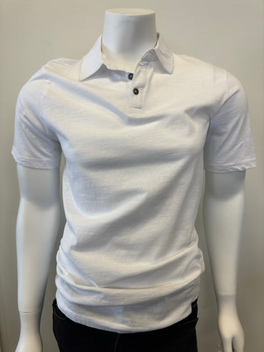 A mannequin wearing the Cotton Polo Men’s in white, featuring a classic collar and short sleeves, with three dark buttons on the placket, stands against a plain, light-colored background. The outfit is completed with dark pants from Silver Jeans Co., showcasing a casual yet stylish look.