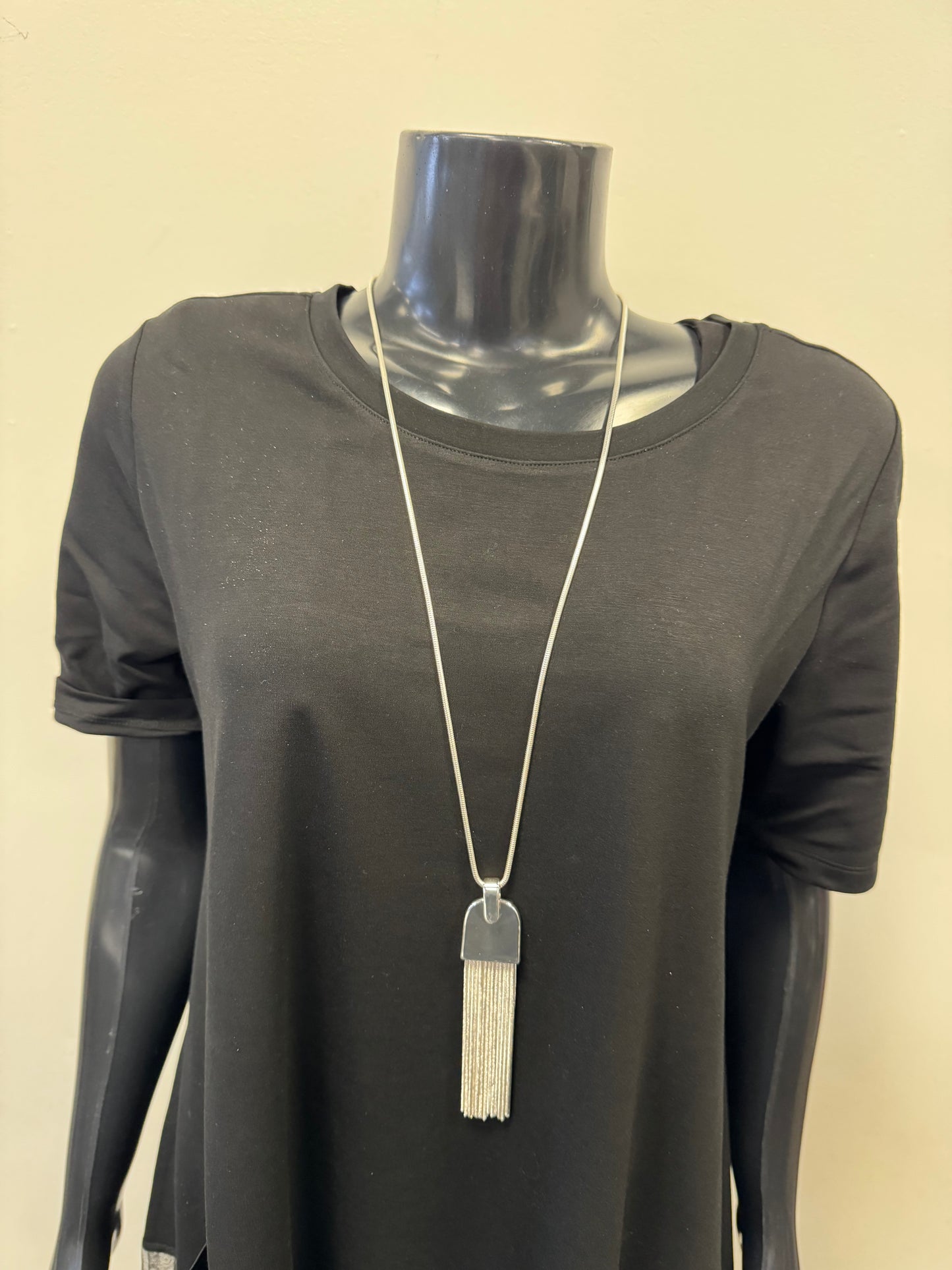 A black mannequin is dressed in a plain black short-sleeve top, adorned with a long fine chain necklace featuring the "Red Coral - Silver Pendant" by Posies Flowers & Fashion Inc. The background is a plain, light-colored wall.