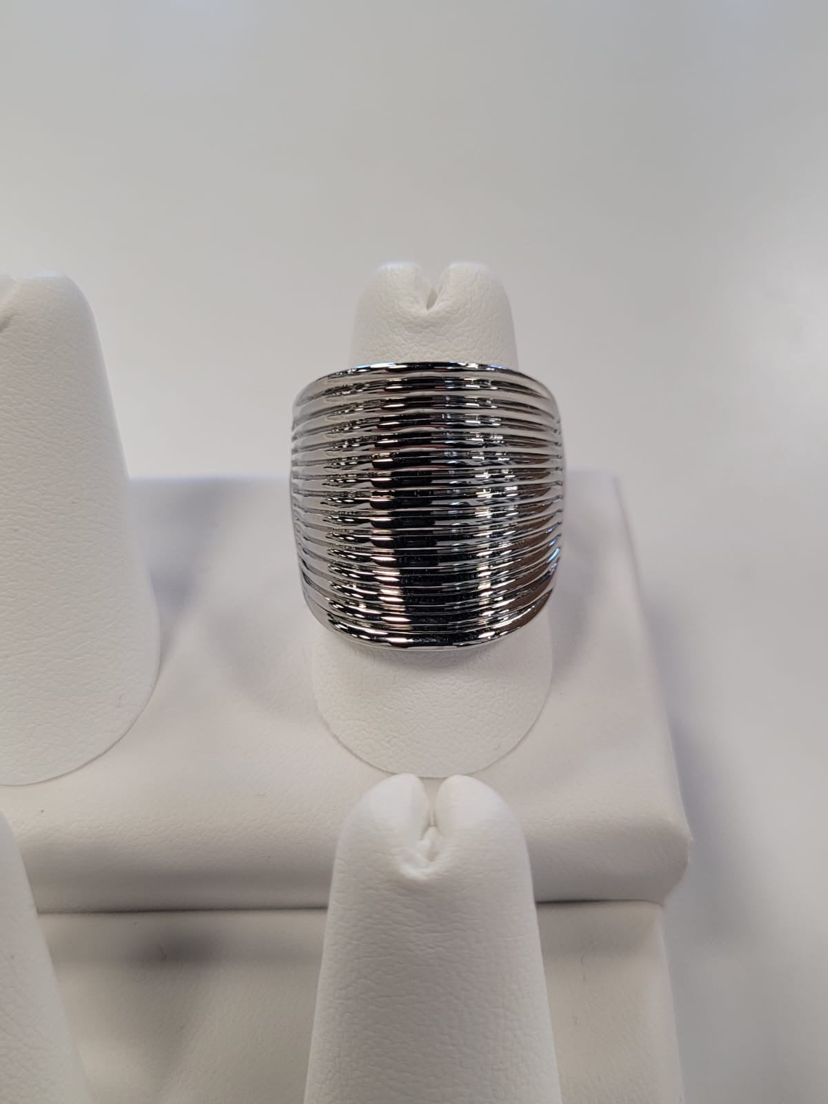 A silver ring with a ribbed texture is displayed on a white, padded ring stand. Known as the Cathy-27 Adjustable Ring from Elise Accessories, it features a wide, adjustable band and a reflective surface that catches the light to highlight its textured design. The backdrop is a plain white surface, emphasizing this versatile accessory.