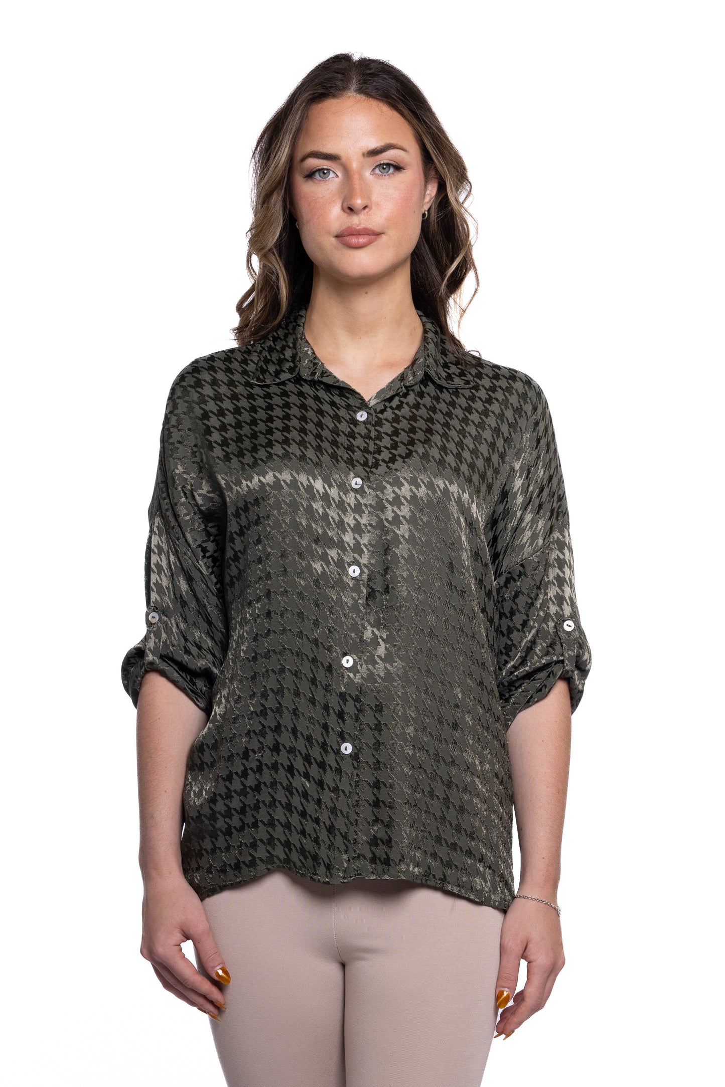 A woman stands against a white background, wearing the Button Top Military - Eternelle from ETERNELLE. The dark green, button-up shirt, adorned with chic button detailing and rolled-up sleeves, is crafted from 100% viscose. She has loose, wavy hair and gazes directly at the camera with a neutral expression. The stylish shirt contrasts beautifully with her light-colored pants.