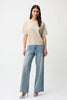 A woman with long, straight brown hair and a neutral expression wears the Joseph Ribkoff Sequins Yarn Short Sleeve Sweater 261917 against a plain white background. She pairs it with light blue wide-leg jeans, silver heels, and hoop earrings.