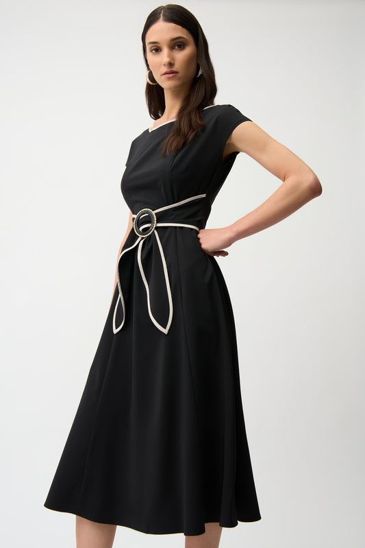A woman wears the Joseph Ribkoff Stretch Woven Color Block Fit and Flare Dress 261051, featuring short sleeves, a knee-length flared skirt, and a contrasting sash belt with a large circular buckle. She stands against a plain background.