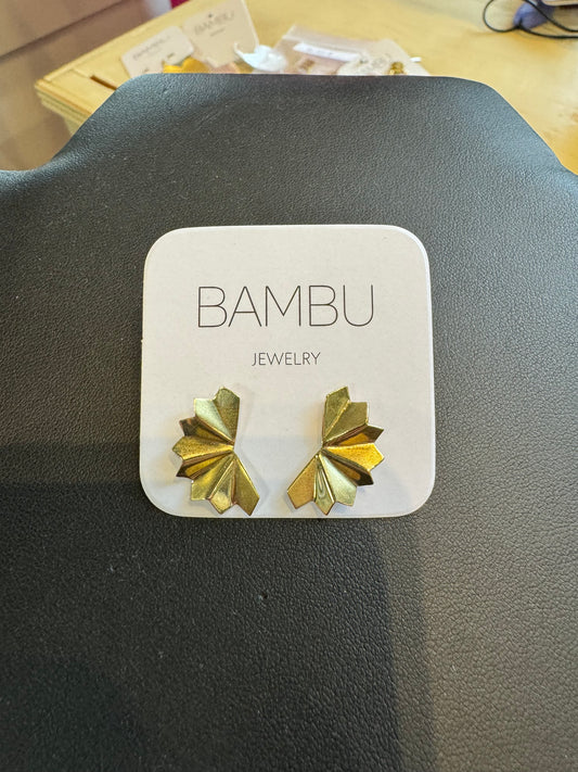 A pair of gold palm earrings, featuring a fan-like palm leaf design, is displayed on a white card labeled "BAMBU Jewellery." The "Gold Palm Fan - BAMBU" earrings are placed on a dark, textured surface.