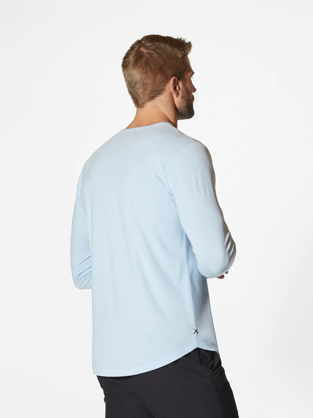 A light blue AO Long Sleeve Curve-Hem Tee by CUTS showcases a simple and clean design. This Signature-fit piece features a small black tag with white text near the neckline inside the back, and a small black X logo stitched near the bottom left side. Made from PYCA Pro fabric, it feels soft and smooth to the touch.