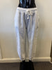The black mannequin displays Bella Amore's Pants Linen 20836, highlighting designer craftsmanship. Made in Italy, these white pants feature an elastic waistband, side pockets, and ankle cuffs against a plain off-white wall.