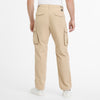 A person is seen from the rear wearing RAGWEAR's vegan streetwear, specifically the MERLY PANTS 2512-55004-6018. These ethical beige cargo pants have large side pockets with button flaps, complemented by white sneakers, set against a plain white background.