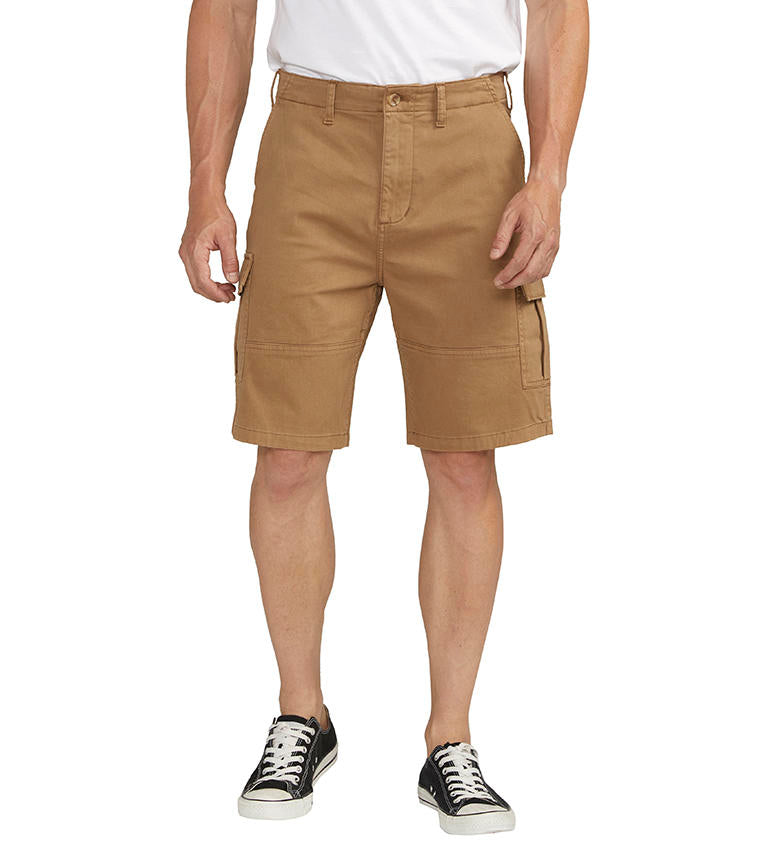 A man stands against a plain background wearing a dark gray t-shirt with a chest pocket, relaxed fit CARGO SHORT DESERT styled by Silver Jeans Co. (product code: M53151CBT639), and black sneakers with white soles. He appears to be adjusting his shirt with his right hand.