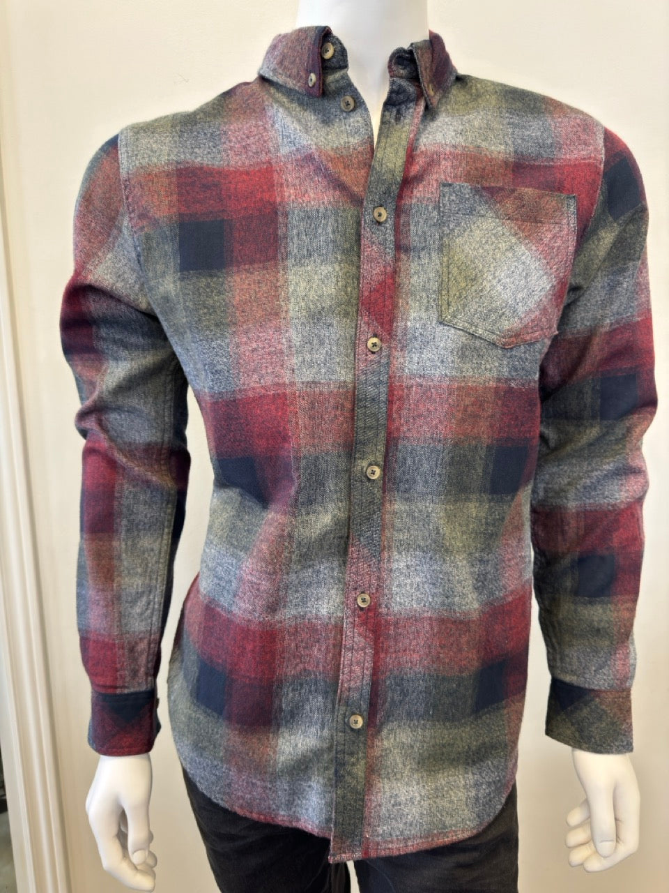 The mannequin is showcasing the Shirt Long Sleeve - BURGUNDY, a button-up flannel with a plaid pattern in shades of red, green, gray, and blue. Expertly paired with denim from Silver Jeans Co., this shirt boasts a single chest pocket and is displayed with the sleeves down and buttons fastened.