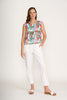 A woman stands against a plain white background wearing the FOIL Its Only Natural Top FO6917 Colour Fusion, paired with white pants and sandals. She has one hand in her pocket and a neutral expression.