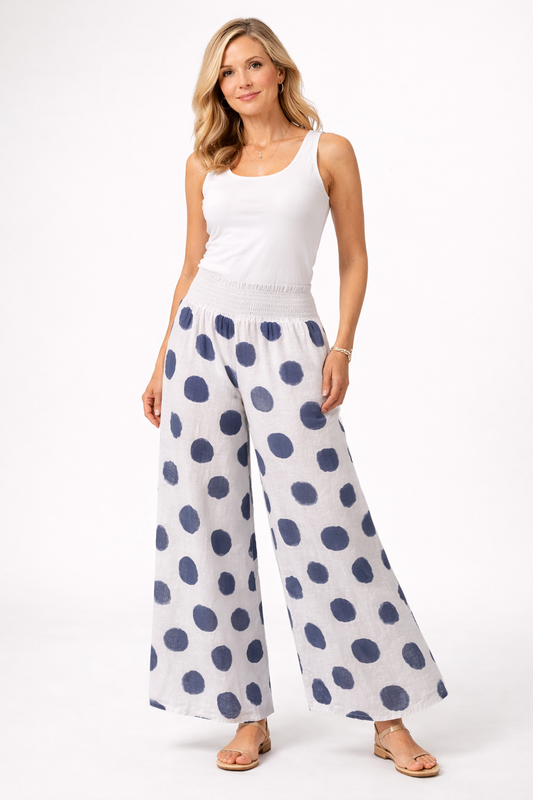 A woman with long blonde hair stands confidently against a white background, wearing Bella Amore Linen Pant 30201 White and a sleeveless top, paired with sandals. Made in Italy, her look is relaxed and stylish.