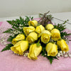 A bouquet of 1 Dozen Yellow Roses Freshcut by Posies Flowers & Fashion, featuring baby's breath and lush greenery, elegantly displayed on a pink surface against a plain white wall.