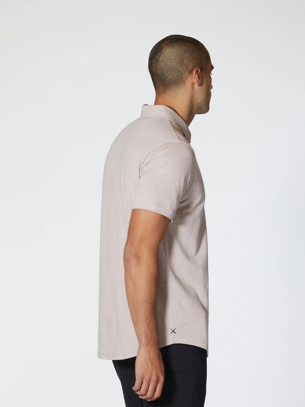 The Universal COZ Polo - CURVE HEM, a light pink short-sleeved shirt by Once We Were Warriors, is neatly laid out. Crafted from Pima Cotton, it features a two-button placket and a small, subtle logo near the bottom hem on the left side. The fabric has a slightly textured appearance and 4-way stretch, giving it an athletic feel while maintaining its clean, minimalist style.