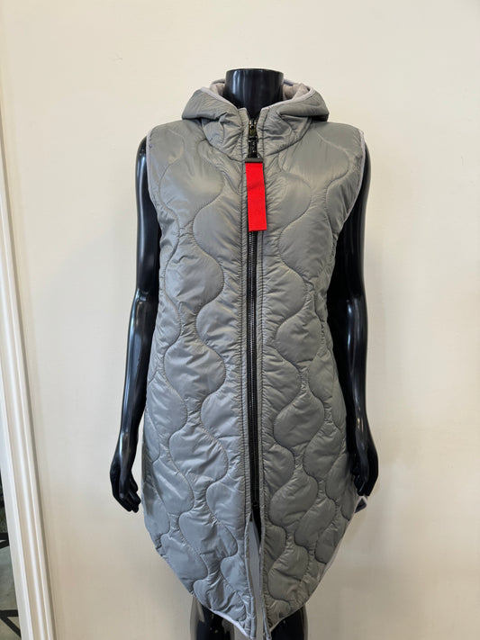 A black mannequin showcases the Vest Light by Catherine Lillywhite, a chic sleeveless and hooded gray quilted piece. The stylish vest features a distinctive wavy stitch pattern and a front zipper adorned with a red tag. An off-white wall serves as a simple backdrop for the display.