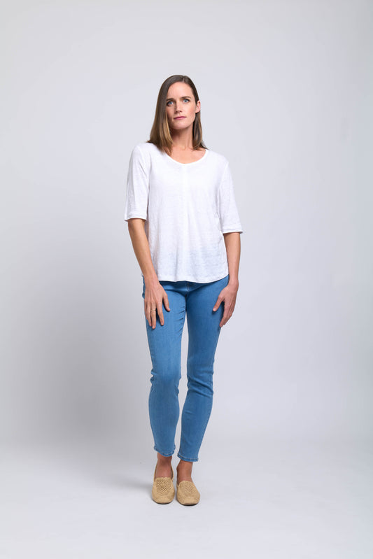 A woman with straight brown hair stands against a white background, wearing the Heroine Top CFO7824 by FOIL, paired with light blue jeans and beige shoes. She has a neutral expression and her arms rest by her sides.