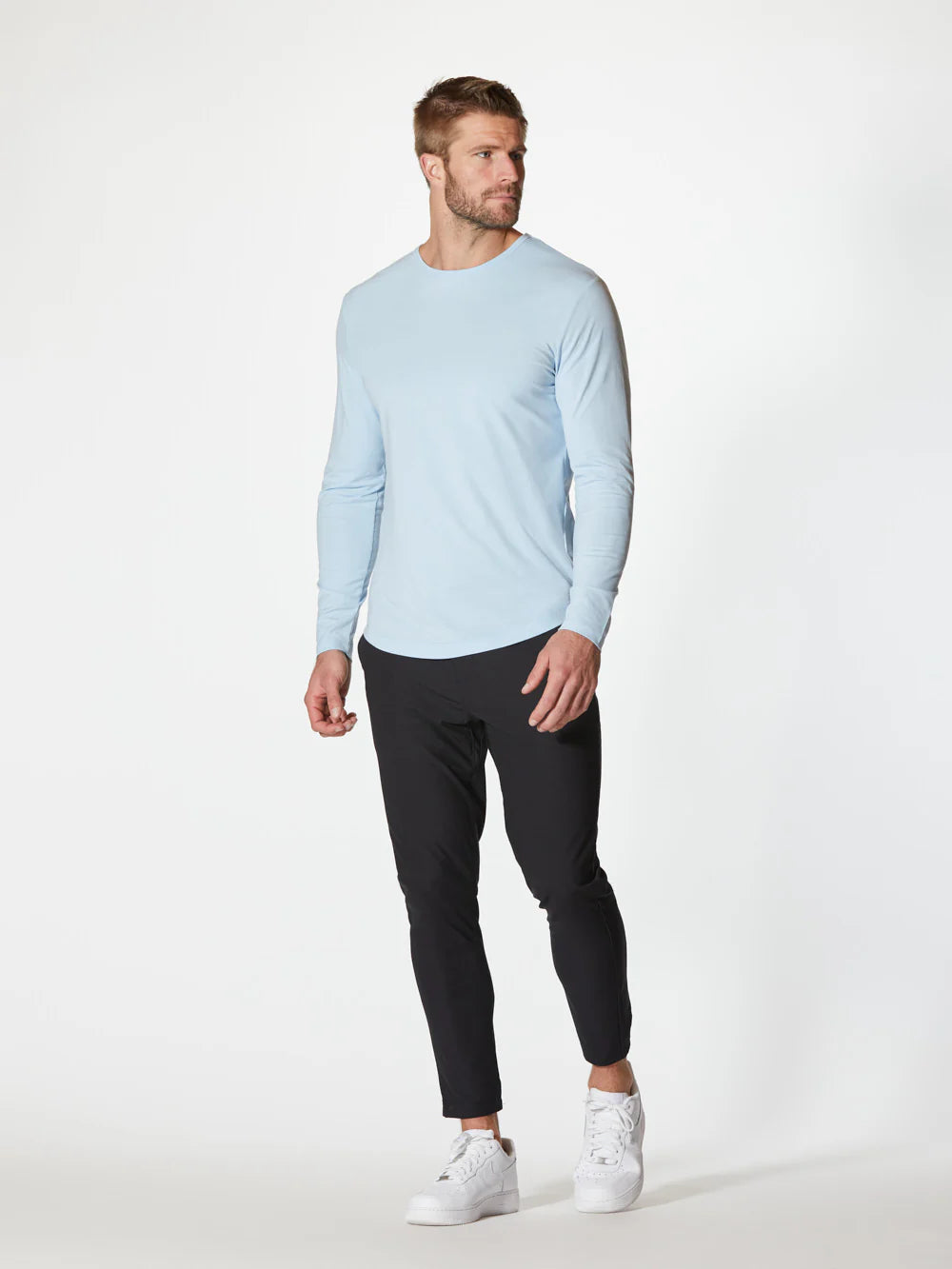 A light blue AO Long Sleeve Curve-Hem Tee by CUTS showcases a simple and clean design. This Signature-fit piece features a small black tag with white text near the neckline inside the back, and a small black X logo stitched near the bottom left side. Made from PYCA Pro fabric, it feels soft and smooth to the touch.