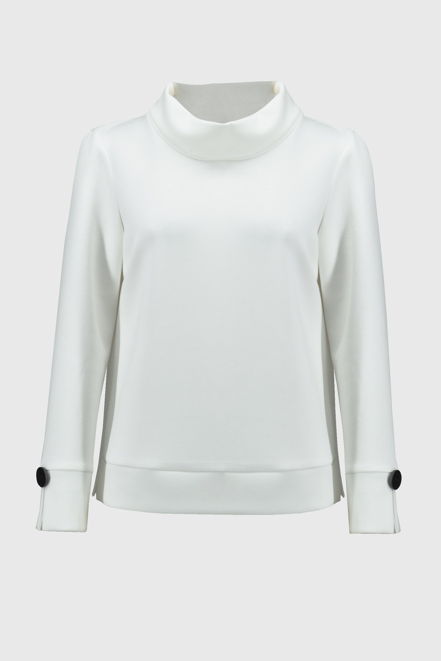 A woman with curly hair wears a loose-fitting, long-sleeved white Scuba Jersey Boxy Top 244129 by Joseph Ribkoff. The top, featuring button details on the sleeves, lends a boxy silhouette. She stands in front of a plain background, looking slightly downward with a neutral expression.