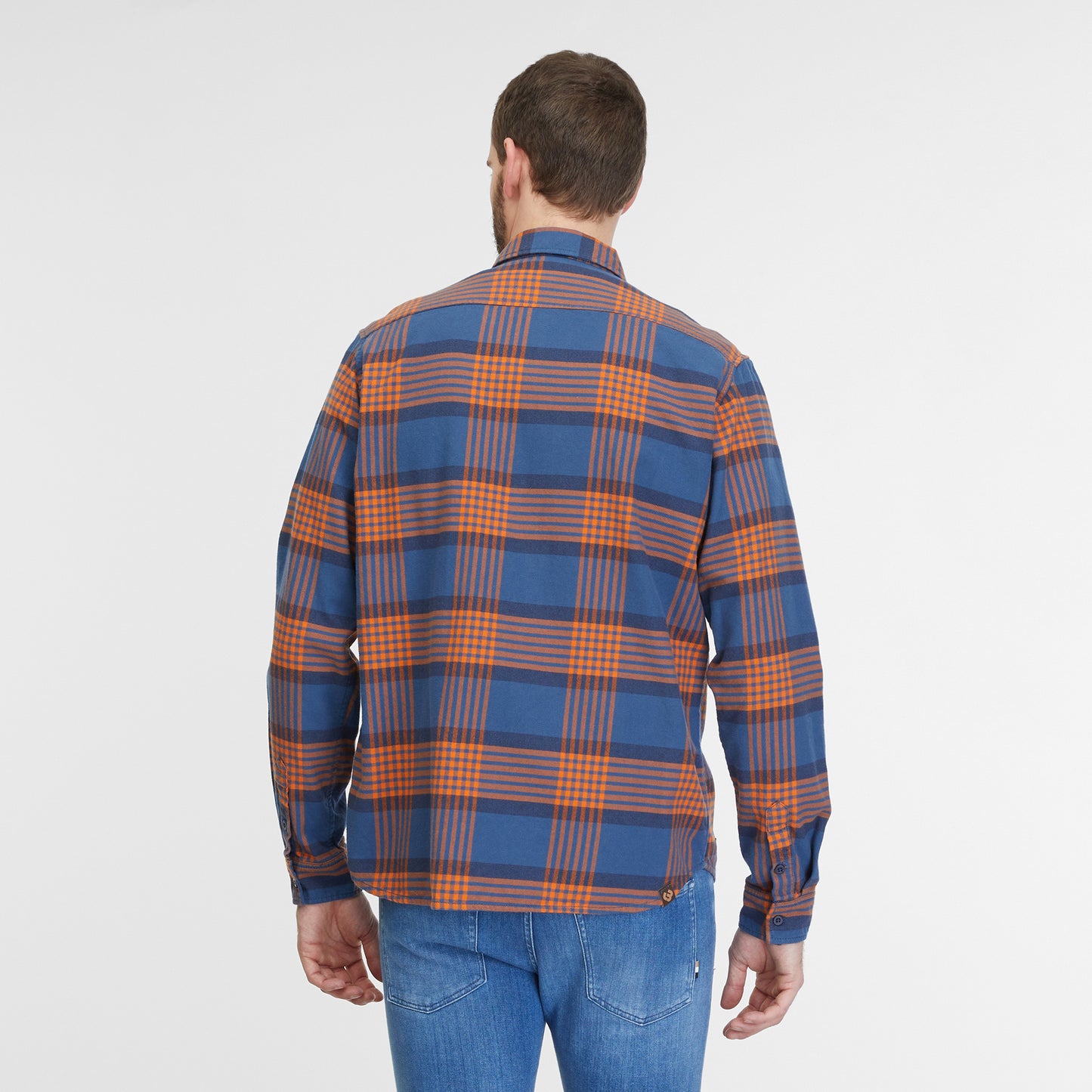 A man with a beard is standing against a plain white background. He is sporting a blue and orange plaid "Shirt Checki Blue 2422-40003-2040" by RAGWEAR, a vegan streetwear cotton flannel shirt with two chest pockets, paired with blue jeans. He is looking straight at the camera with a neutral expression.