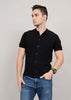 A person with short hair stands against a plain background, looking to the side in a fashion-forward wardrobe, wearing a sleek HEDGE Sweater Knit Button Shirt Short Sleeve 56MS311S and blue jeans with a watch on their left wrist, effortlessly merging style with simplicity.