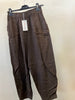 The Pant 100% Linen Chocolate by Paolo Tricot, featuring a loose fit and elastic waistband, hangs on a black hanger with a white tag attached. The chocolate brown pants are displayed against a plain off-white wall.