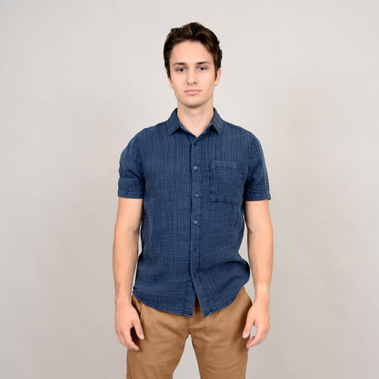 A young man stands against a plain light background, wearing the HEDGE Gauze Short Sleeve Shirt Navy 56MW102S and tan pants—a relaxed, effortless summer look. He faces the camera with a neutral expression, arms resting at his sides.