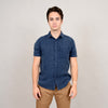 A young man stands against a plain light background, wearing the HEDGE Gauze Short Sleeve Shirt Navy 56MW102S and tan pants—a relaxed, effortless summer look. He faces the camera with a neutral expression, arms resting at his sides.