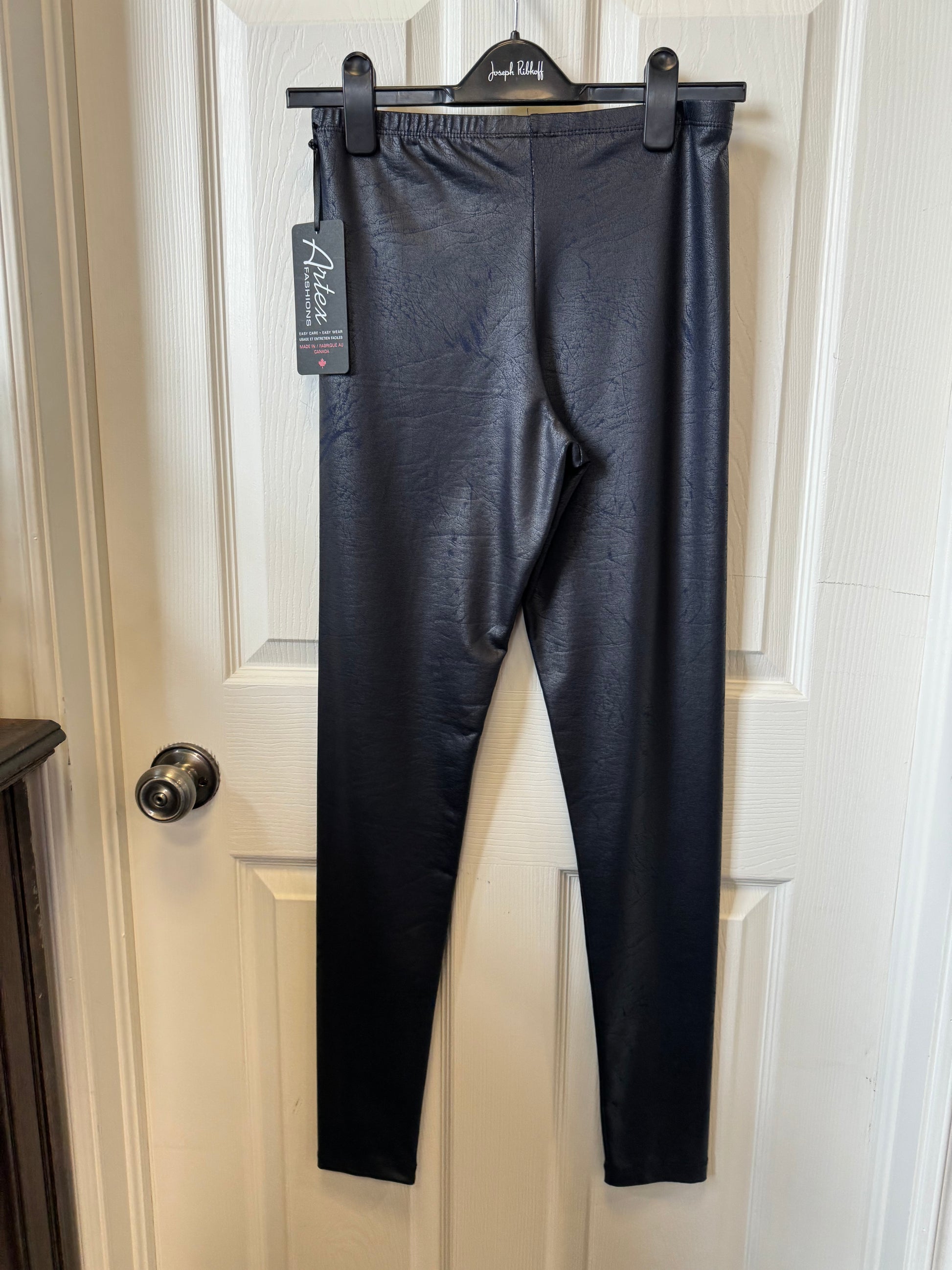 A pair of Dark Navy Leggings by Tribal hang on a black hanger against a white door. The tag on the leggings reads "Artex Fashions - Dark Navy Legging 112-9067" and provides product details. The door has a silver-colored doorknob, and the overall indoor setting promises ultimate comfort and style.