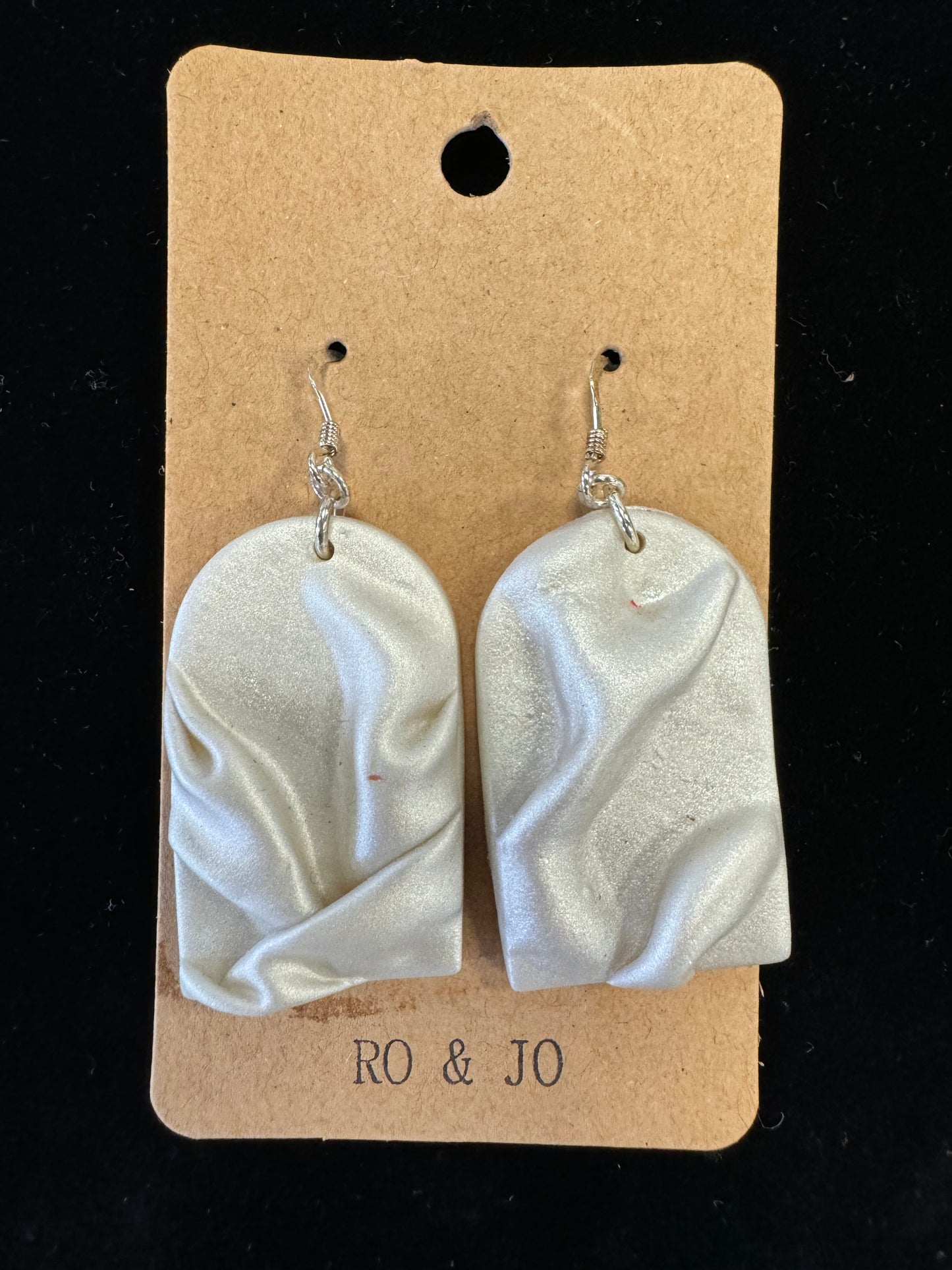 A pair of light gray, handmade Ro&Jo Earrings 433 with a wavy, textured design hangs on hooks attached to a brown cardboard backing. The backing has a small hole at the top for display purposes and the text "RO&JO" printed at the bottom.