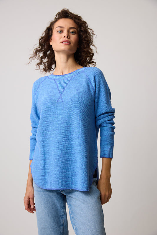 A person with curly hair wears the Skyler Sweatshirt 80049 from Parkhurst Cotton Country in light blue, made of 100% cotton, paired with jeans. They stand against a plain backdrop, gazing upward calmly.