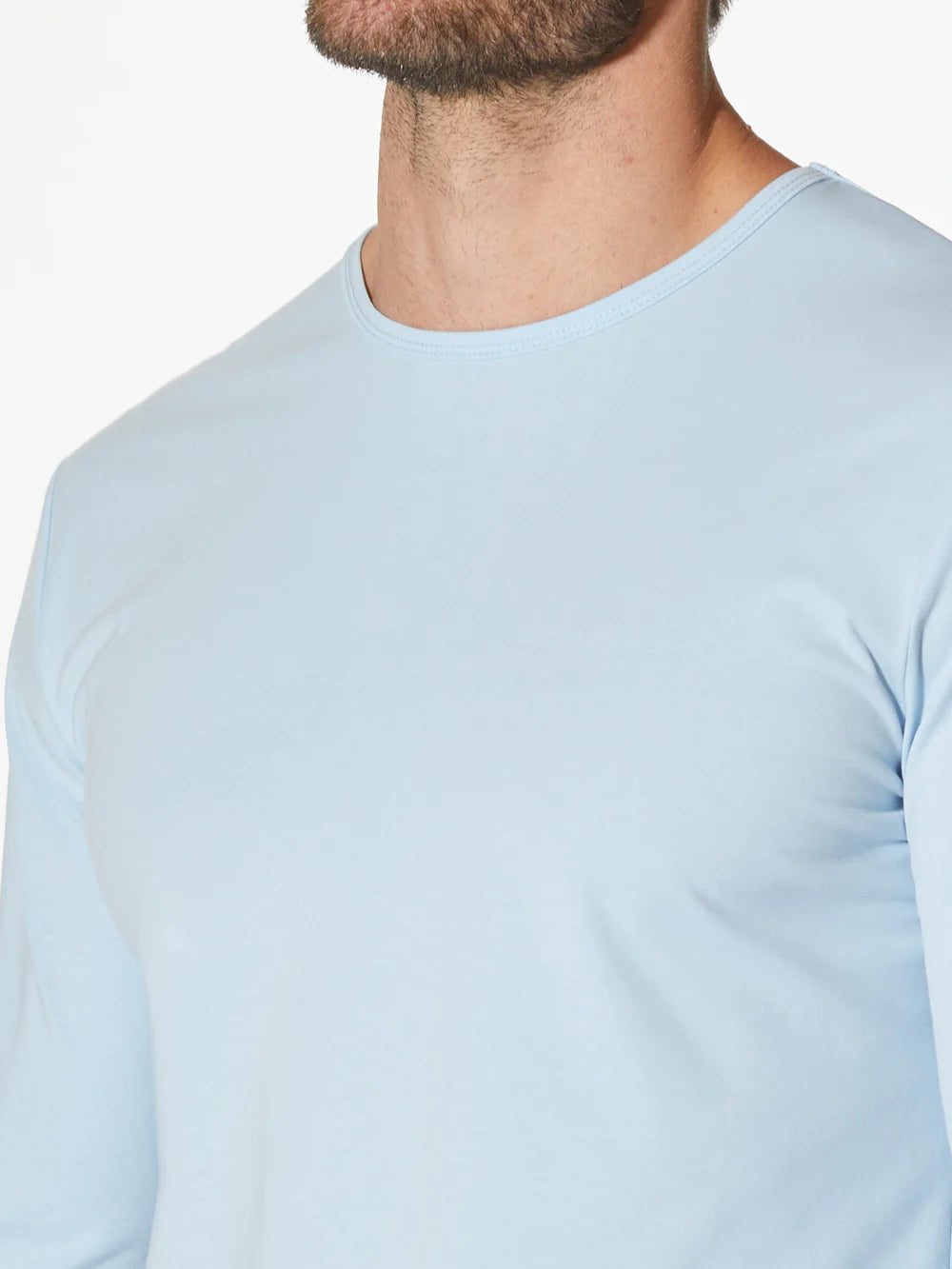 A light blue AO Long Sleeve Curve-Hem Tee by CUTS showcases a simple and clean design. This Signature-fit piece features a small black tag with white text near the neckline inside the back, and a small black X logo stitched near the bottom left side. Made from PYCA Pro fabric, it feels soft and smooth to the touch.