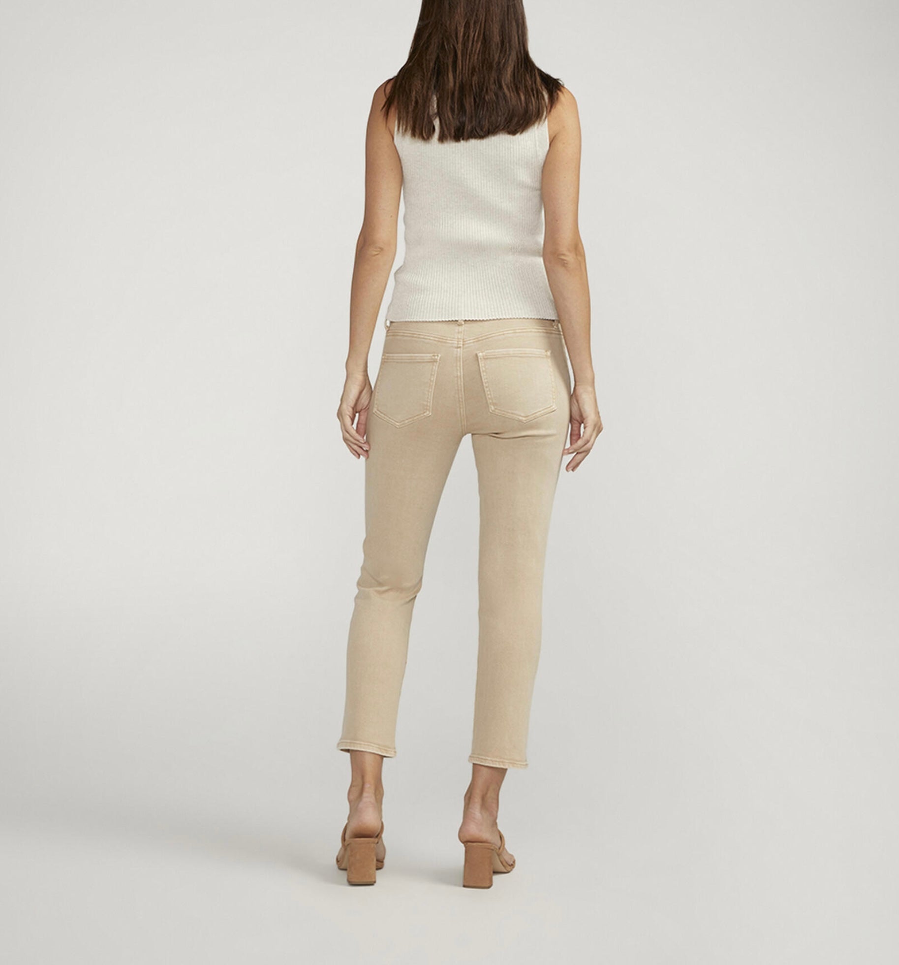 A person stands wearing a sleeveless, cream-colored ribbed top paired with JAG's Cassie Mid Rise Cropped Pants in beige. They are also wearing beige open-toe heels. The background is plain white, and the person's hands rest beside their hips.