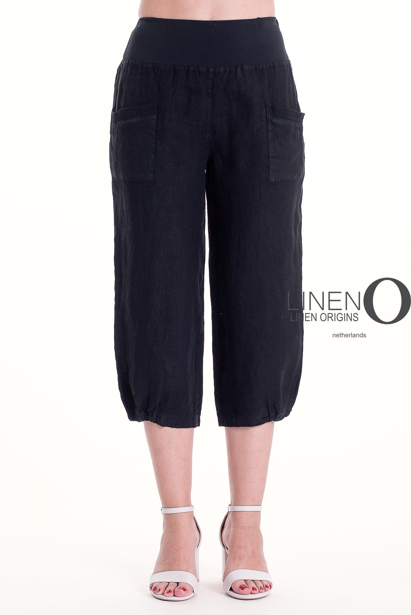 A person stands against a white background wearing LinenO's French Linen Capri PT878-74 Nero, featuring premium linen, front pockets, and an elastic waistband, paired with white high-heeled sandals.