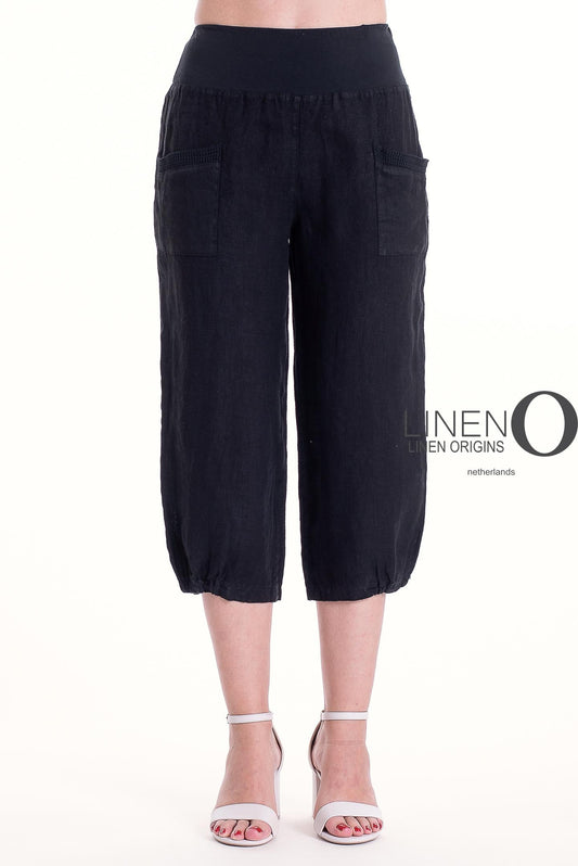 A person stands against a white background wearing LinenO's French Linen Capri PT878-74 Nero, featuring premium linen, front pockets, and an elastic waistband, paired with white high-heeled sandals.