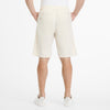A person is seen from the back wearing RAGWEAR's LONGYZ 2512-50014-7010 light beige shorts made of a cotton linen blend with two back pockets, paired with white sneakers and a plain white T-shirt, all against a white background, showcasing effortless sustainable fashion charm.