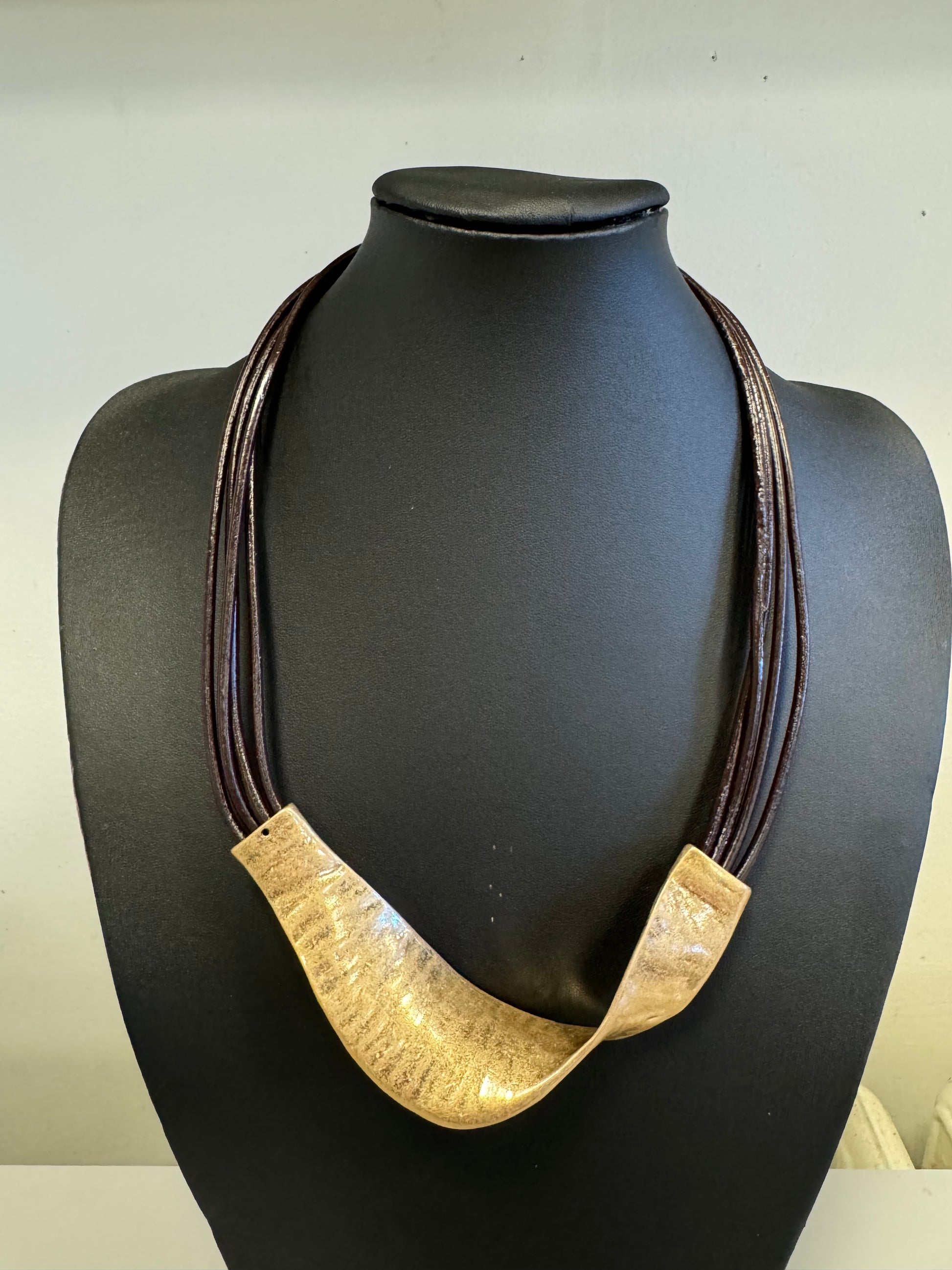 The Roxanne 27 Necklace from Elise Accessories, featuring multiple dark strands and a prominent curved metallic centerpiece, is elegantly presented on a black bust.