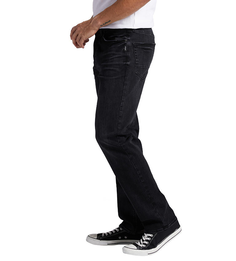 A person wearing a pair of Machray Athletic Fit Straight Leg Silver Jeans M63410CBB532 from Silver Jeans Co. and black sneakers with white laces. The individual is also dressed in a white t-shirt, and the image shows them from the shoulders down, standing against a white background.