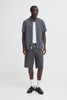 A man stands against a plain white background wearing the BLEND BARNY SHIRT 20720749-194011, a checked men's cotton shirt, over a white T-shirt with dark denim shorts, white socks, and black loafers.