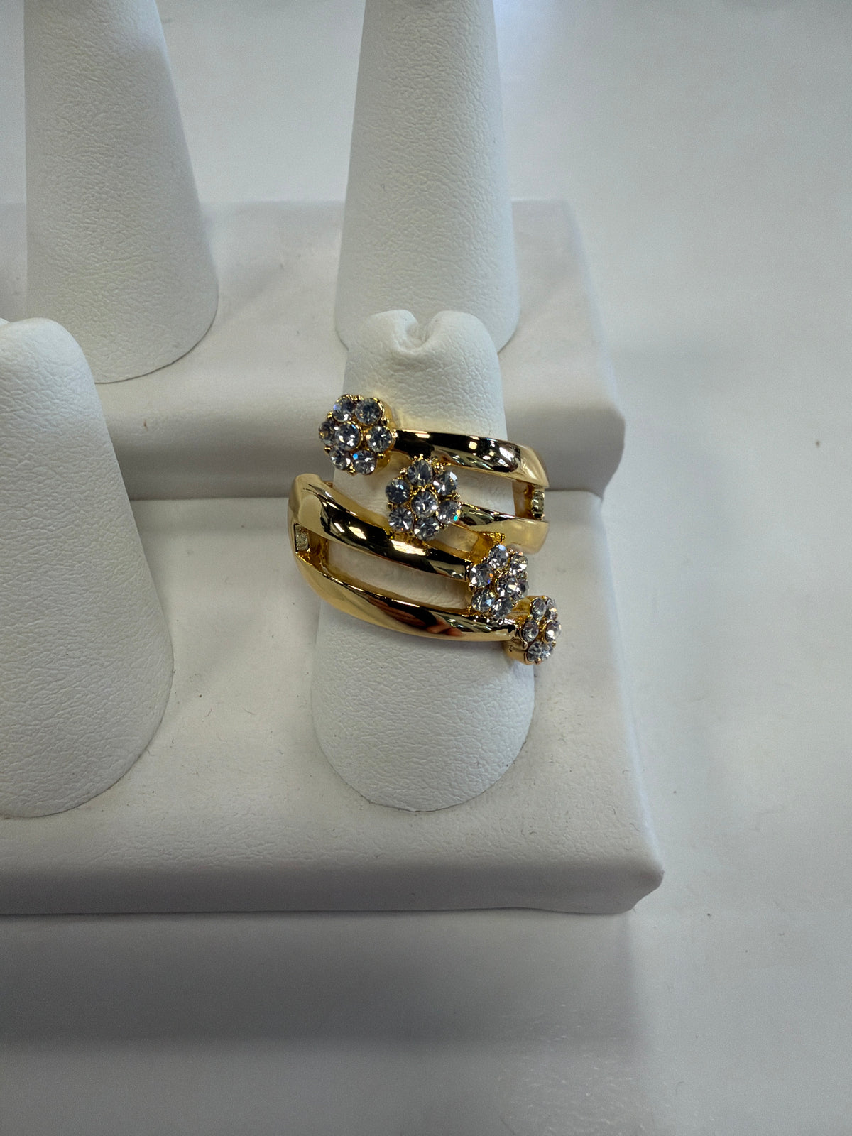 Jenna 86 Ring by Elise accessories, a gold bypass ring on a stretch band featuring three flower-shaped clusters of clear CZ stones.