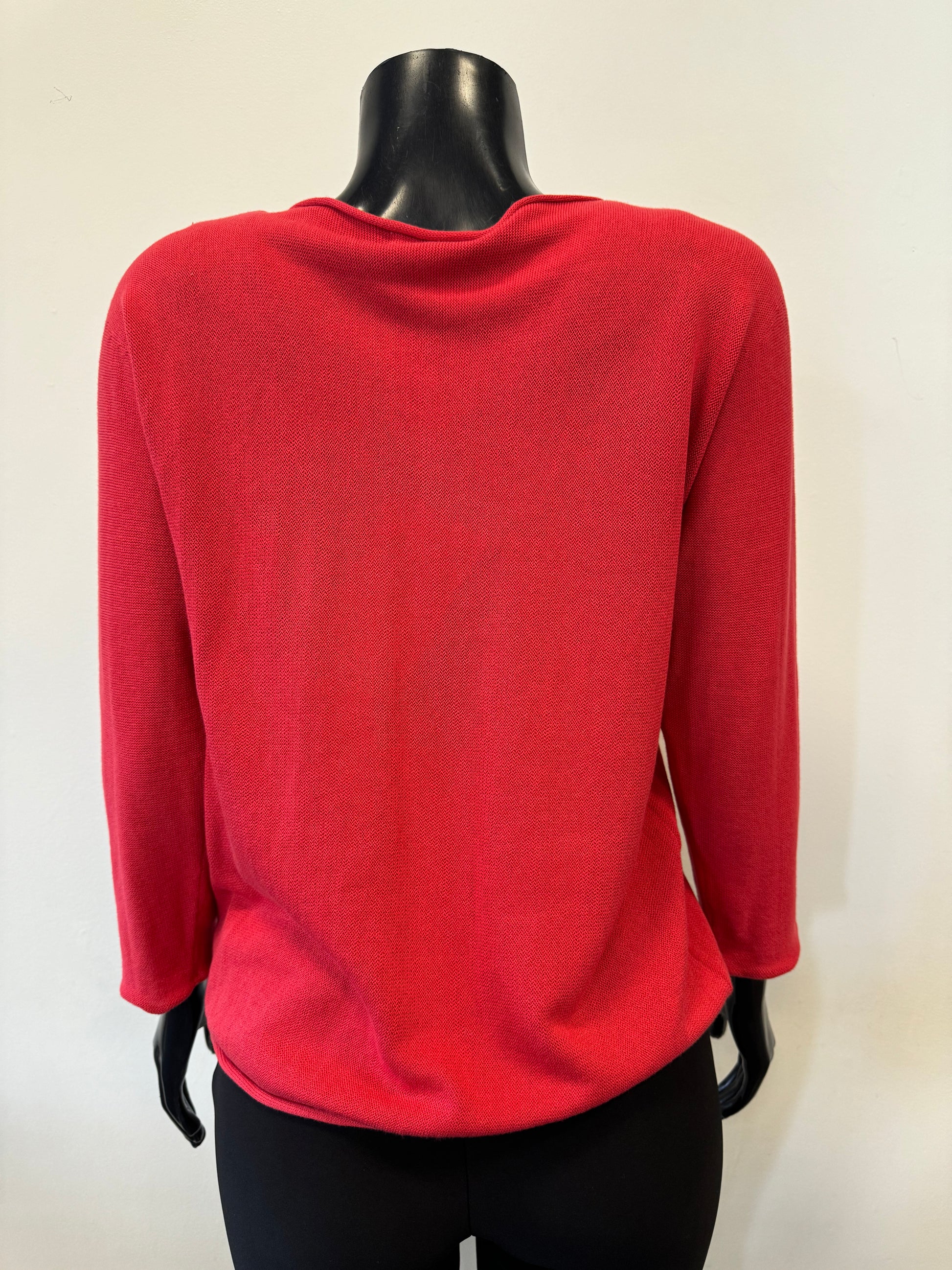 A black mannequin dressed in the ORIENTIQUE Knit Top Long Sleeve - Orientique, a red knit top made from organic cotton, paired with black pants is displayed against a plain white background. The top features a relaxed fit and a slightly rounded hem, with the mannequin's head and hands not shown.