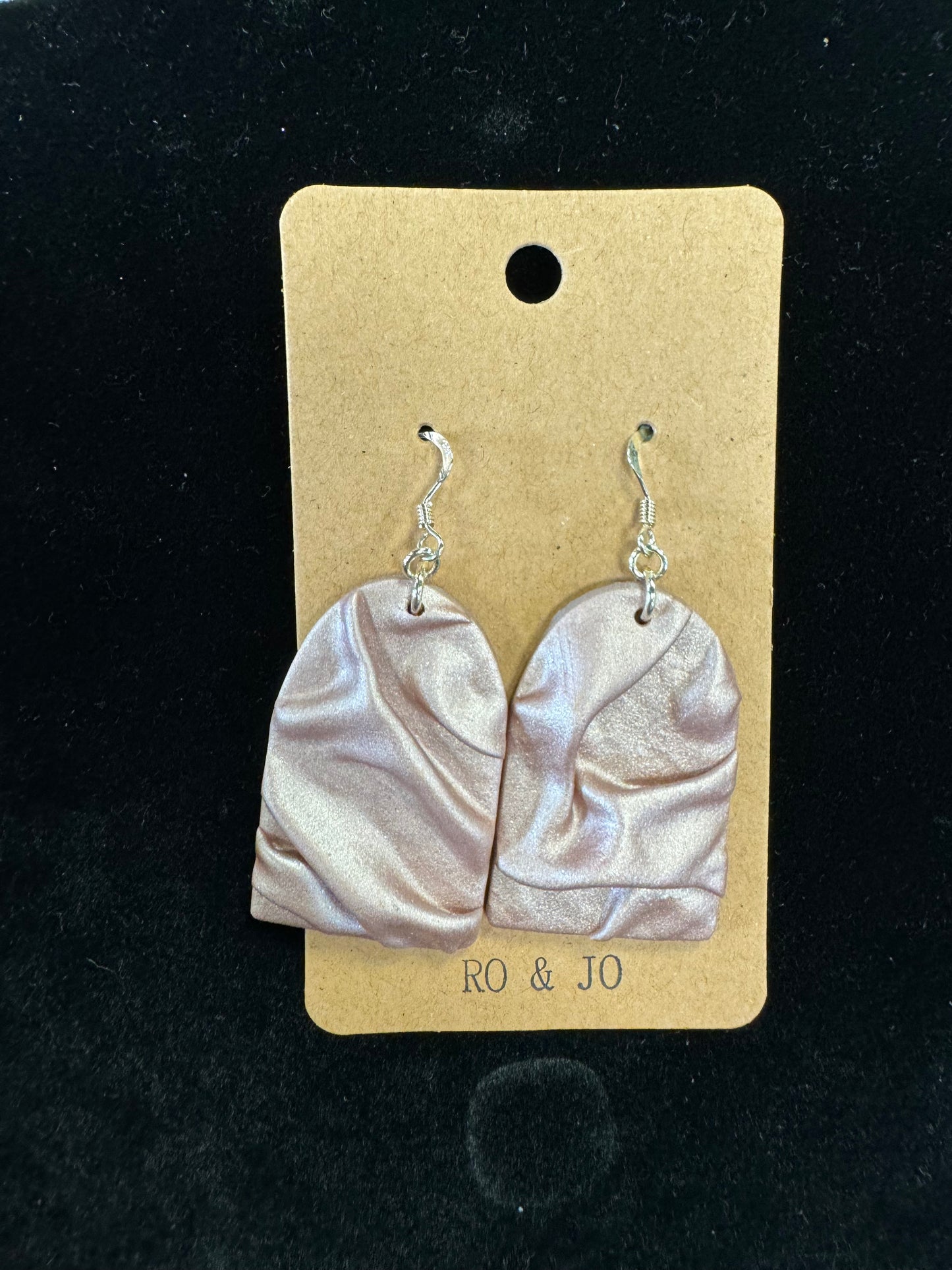 A pair of handmade Ro&Jo Earrings 439 with a marbled design in shades of beige and light brown, displayed on a brown cardboard backing with the brand name "RO&JO." Crafted from polymer clay, the earrings feature textured, abstract shapes and are attached to silver hooks.