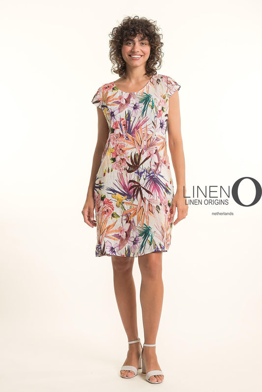 A smiling person with curly hair wears the French Linen Dress TP1758P-159 Carne by LinenO, featuring premium linen and a colorful floral and leaf print. They stand against a plain background with the "LINEN ORIGINS netherlands" logo on the right.