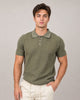 A young man with short brown hair wears the HEDGE Knit Polo Light Olive 56MS372S and light beige pants, standing against a plain light gray background with one hand in his pocket, looking at the camera.