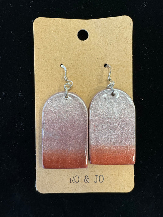 A pair of handmade Ro&Jo Earrings 429 is displayed on a cardboard holder with the label "RO&JO." The rectangular earrings have rounded tops and feature a gradient design that transitions from dark red at the bottom to shimmering silver at the top.