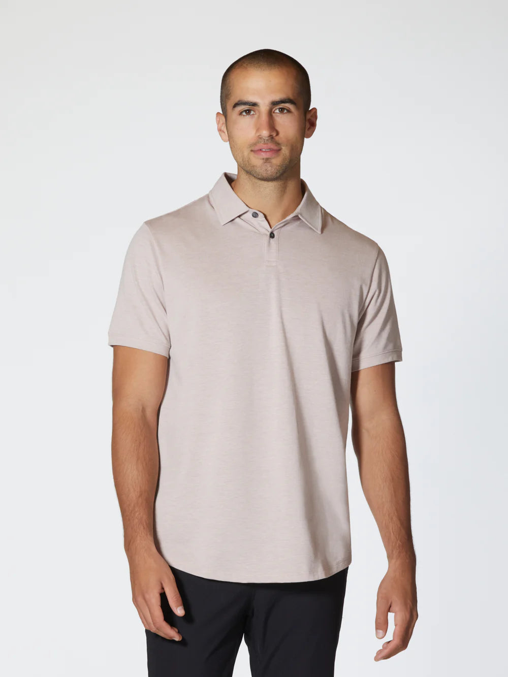 The Universal COZ Polo - CURVE HEM, a light pink short-sleeved shirt by Once We Were Warriors, is neatly laid out. Crafted from Pima Cotton, it features a two-button placket and a small, subtle logo near the bottom hem on the left side. The fabric has a slightly textured appearance and 4-way stretch, giving it an athletic feel while maintaining its clean, minimalist style.