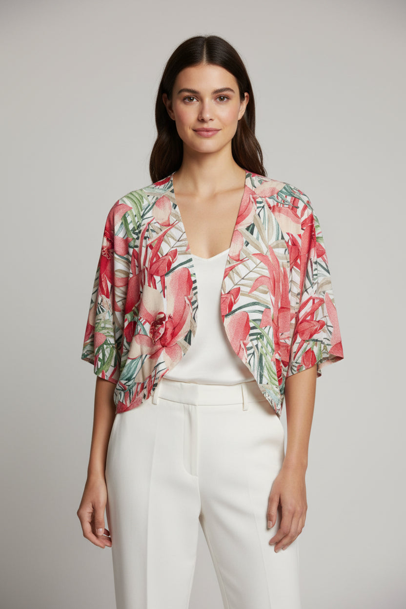 A woman wears the TaraVao Top Megan 5098 with pants and a loose, colorful floral kimono-style jacket in red, green, and pink. She smiles softly against a neutral background. Made in Bali by TaraVao.