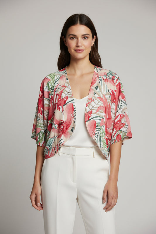 A woman wears the TaraVao Top Megan 5098 with pants and a loose, colorful floral kimono-style jacket in red, green, and pink. She smiles softly against a neutral background. Made in Bali by TaraVao.