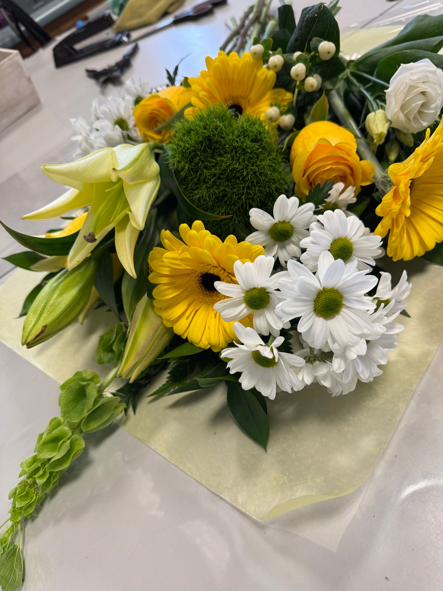 The Whites & Yellows Freshcut by Posies Flowers & Fashion features vibrant yellow gerbera daisies, white daisies, lilies, and green foliage. Depending on flower availability, similar cheerful blooms may be substituted for a beautifully coordinated look.