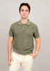 Dressed in a Knit Polo Light Olive 56MS372S by HEDGE, the individual stands against a beige background. With their right hand in their pocket and a neutral expression, the 100% cotton knit of the short-sleeved top enhances their casual elegance alongside light-colored pants.
