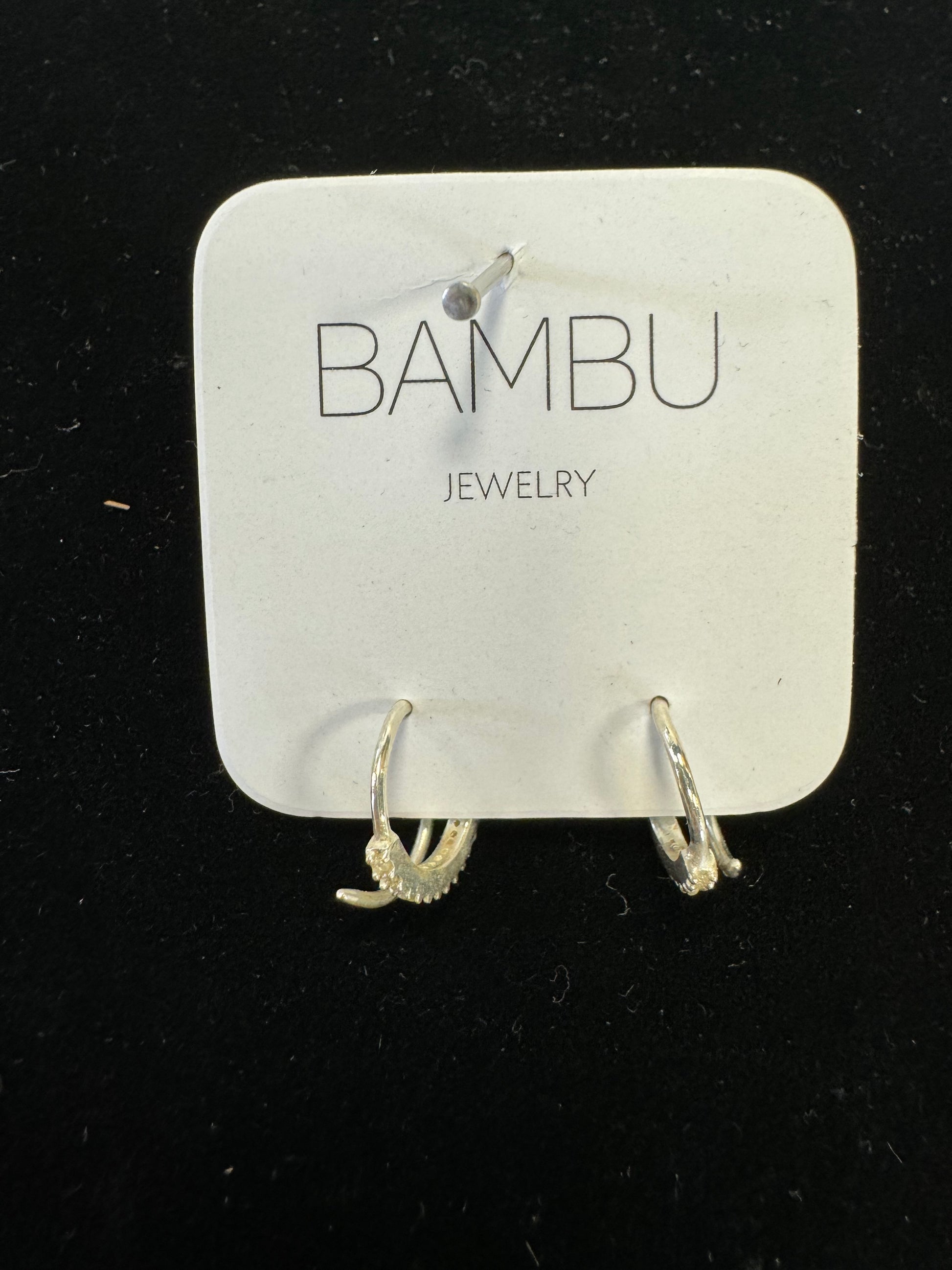 A stunning pair of Gold Embezzled Hoop Earrings from BAMBU Jewellery adorns a white card with "BAMBU JEWELLERY" in gray. These elegant earrings are gold-colored and feature small, clear stones along the front. The card and earrings rest against a dark, textured surface.