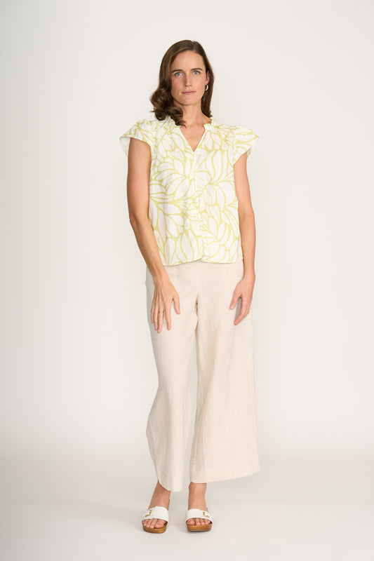 A woman with shoulder-length brown hair and a neutral expression wears the FOIL As a Button Top Silhouette FO8301, featuring a botanical-inspired yellow and white print, paired with beige wide-leg pants and white sandals against a plain white background.