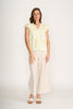 A woman with shoulder-length brown hair and a neutral expression wears the FOIL As a Button Top Silhouette FO8301, featuring a botanical-inspired yellow and white print, paired with beige wide-leg pants and white sandals against a plain white background.
